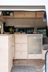 Interior of a BANZ New Zealand camper van featuring light wood cabinetry, a sink, and a small refrigerator