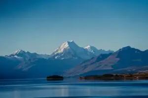 Snow-capped mountains rise above a serene blue lake with a small island