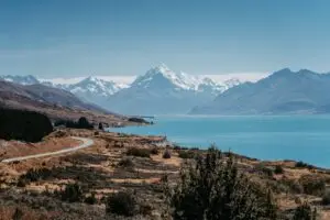Winding road along the turquoise shores of a lake with snow-capped mountains in the background