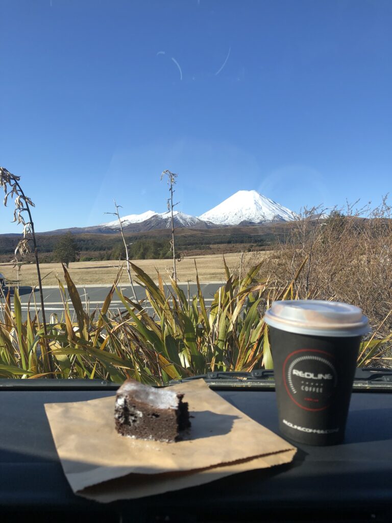 A brownie and Redline Coffee cup on a car dashboard with a snow-capped mountain in the background