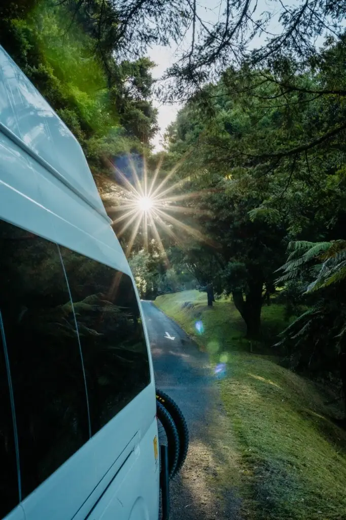 Banz Travelcars Campervan parked on a road in a lush forest with a sunburst shining through the trees
